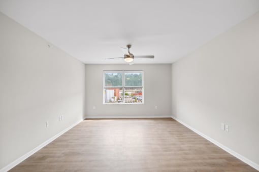 an empty living room with a ceiling fan and a window