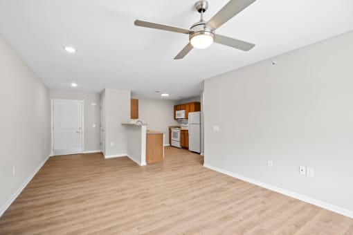 an empty living room with a ceiling fan and a kitchen