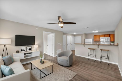 A living room with a white couch, a grey armchair, a wooden coffee table, and a flat-screen TV mounted on the wall.