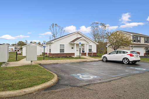 A white car is parked in a parking lot with a building in the background.