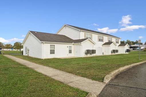 A white house with a brown roof is surrounded by a grassy area.
