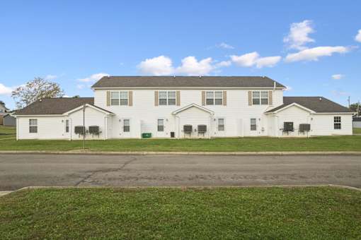 A white two story house with a grey roof and a green lawn in front.
