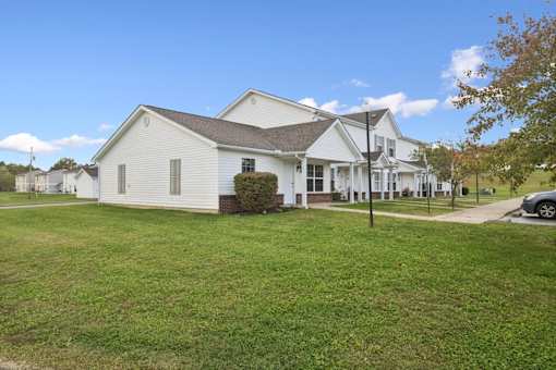 A white house with a brown roof and a green lawn in front.