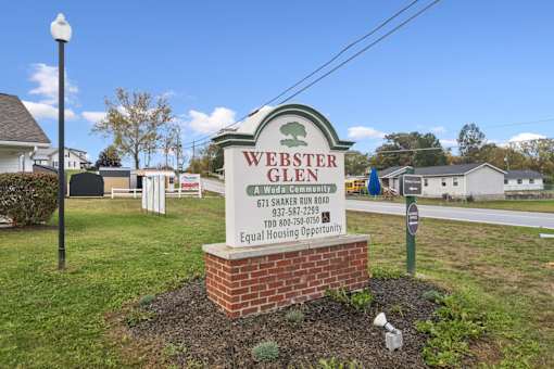 A sign for Webster Glen, a Wada community, is displayed in front of a grassy area.
