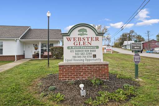 A sign for Webster Glen, a Woda community, is displayed in front of a house.