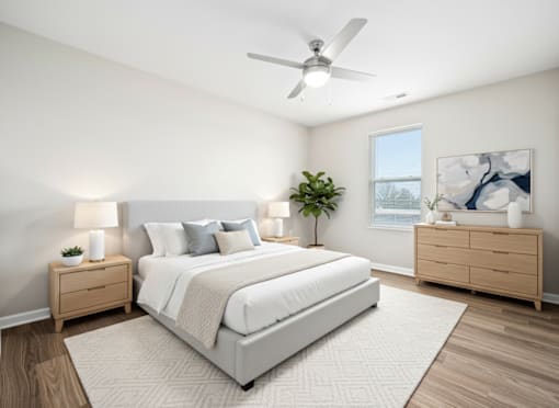 A bedroom with a large bed, a ceiling fan, and a nightstand with a plant on it.