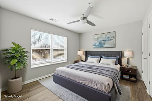 A bedroom with a large bed, a potted plant, and a ceiling fan.