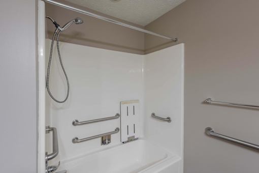 A white shower stall with a silver shower head and grab bars.