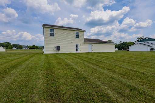 A white house with a brown roof is situated in a grassy field.