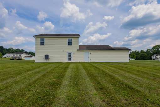 A white barn with a brown roof sits in a grassy field.