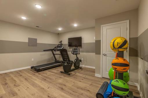 A room with a treadmill, exercise balls and a TV.