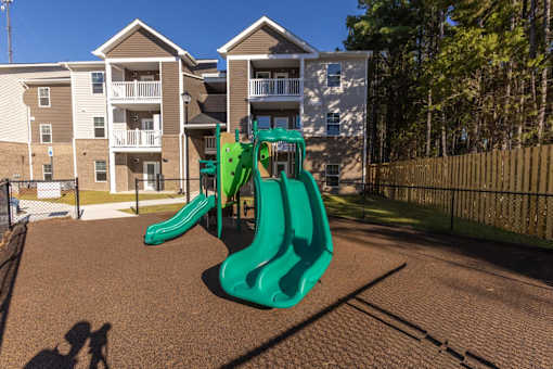 A playground with a green slide in front of apartment buildings.