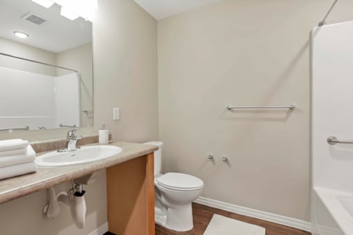 A white toilet sits in a bathroom next to a sink and a bathtub.