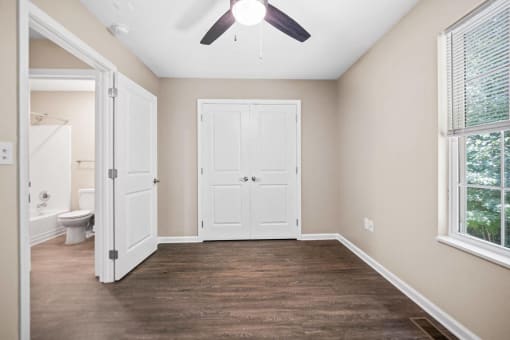 an empty bedroom with a ceiling fan and a door to the bathroom