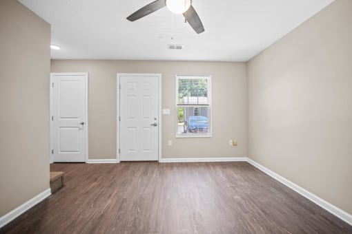 an empty living room with white doors and a ceiling fan