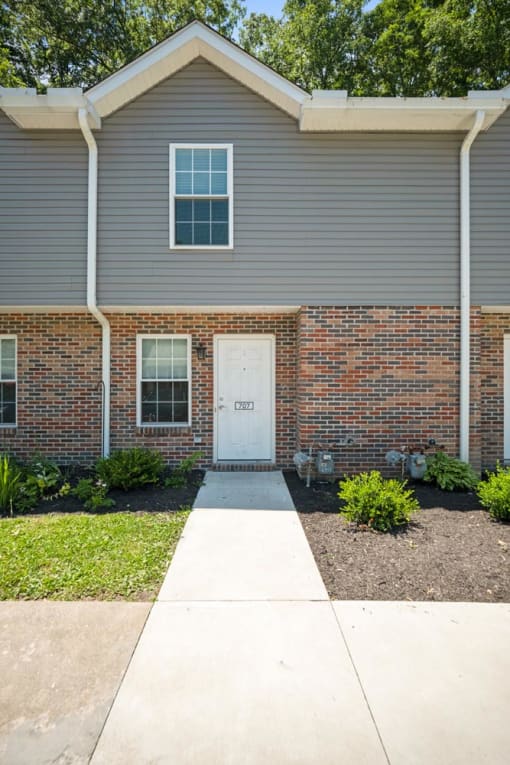 a sidewalk in front of a brick house with a white door