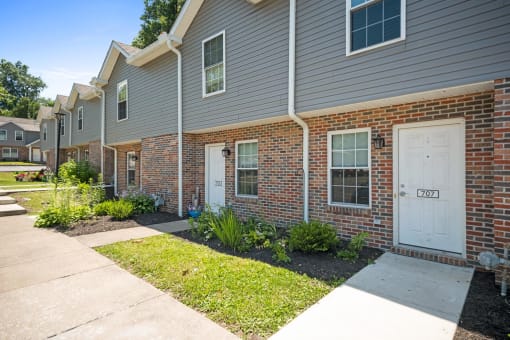 a sidewalk in front of a brick house with white doors