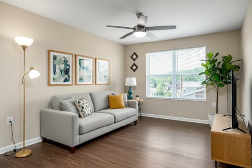 A living room with a grey couch, a floor lamp, a ceiling fan, and a wooden side table.