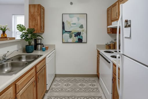 A kitchen with a white fridge, wooden cabinets and a painting on the wall.