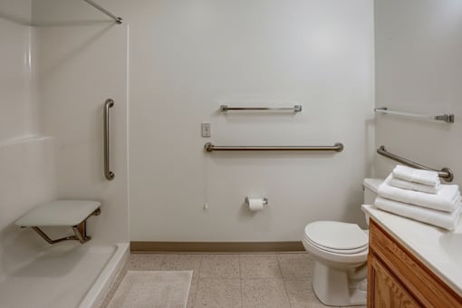 A white toilet sits in a bathroom next to a towel bar and a towel rack.