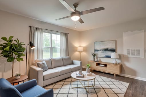A living room with a white sofa, a blue armchair, a wooden coffee table, and a ceiling fan.