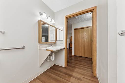 A bathroom with a mirror, sink, and wooden floors.