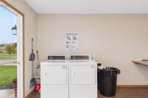 A laundry room with a washer and dryer and a trash can.