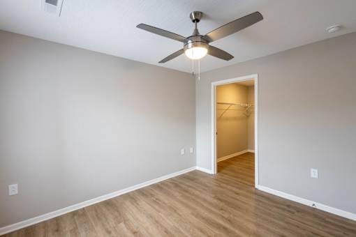 A room with a ceiling fan and light fixture, and a doorway leading to another room.