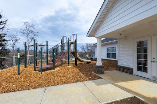 A playground with a slide and swings is in front of a house.