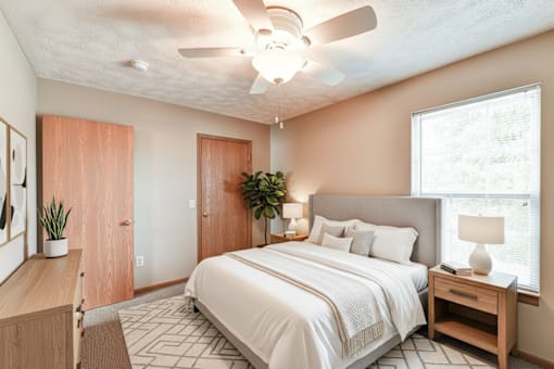 A bedroom with a large bed, a ceiling fan, and a window with a view of trees outside.