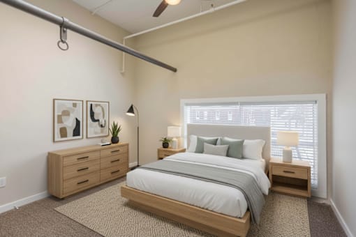 A bedroom with a bed, nightstand, and a dresser with a plant on top.