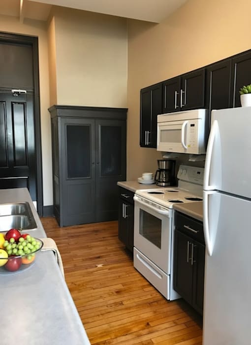 A kitchen with a white refrigerator, black cabinets, and a wooden floor.