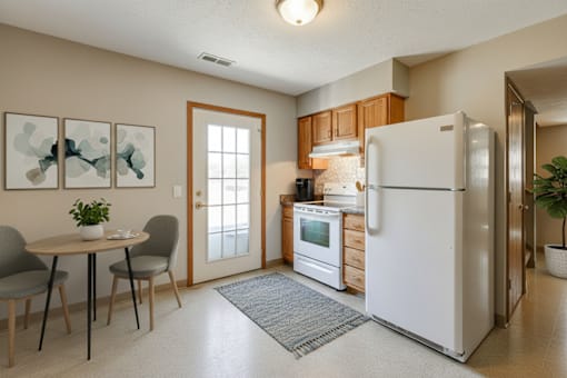 A kitchen with a white refrigerator, a dining table with two grey chairs, and a rug on the floor.