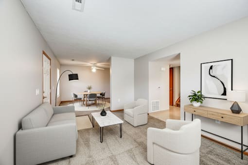 A living room with a grey couch, a white chair, a coffee table, and a painting on the wall.