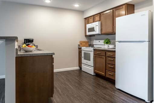 A kitchen with a white refrigerator, brown cabinets, and a counter with a bowl of fruit and a coffee maker.
