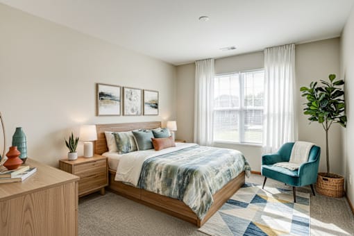 A bedroom with a bed, a chair, a plant, and pictures on the wall.