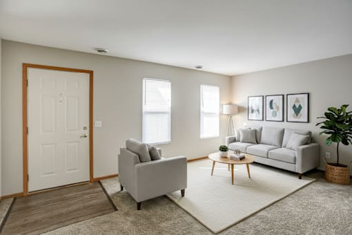 A living room with a grey couch, a grey armchair, a wooden coffee table, and a white door.