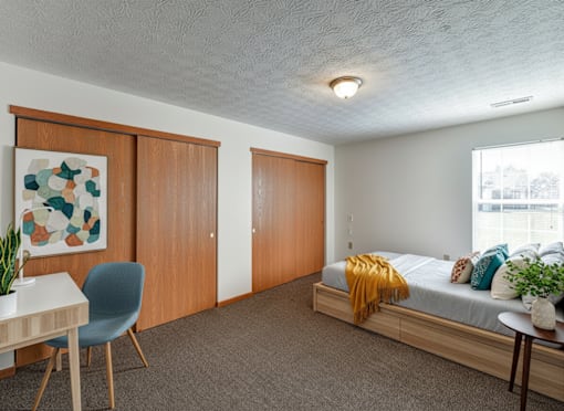 A bedroom with a bed, a chair, a table, and a painting on the wall.