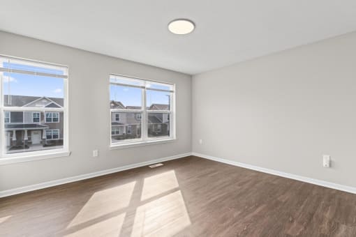 an empty living room with a hardwood floor and three windows