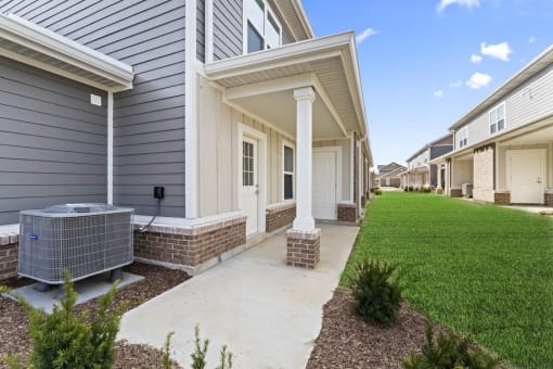 a walkway leading to a house with a yard and a cooling unit