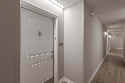 A white door with a keyhole is on the left and a hallway with a light on the right.