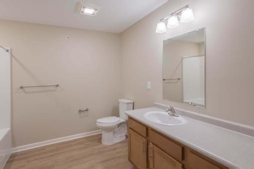A bathroom with a toilet, sink, mirror, and a shower.