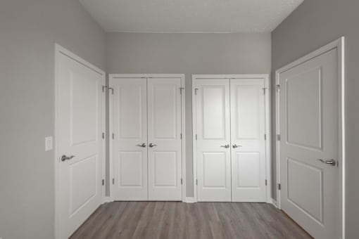 A room with four white doors and wooden floors.