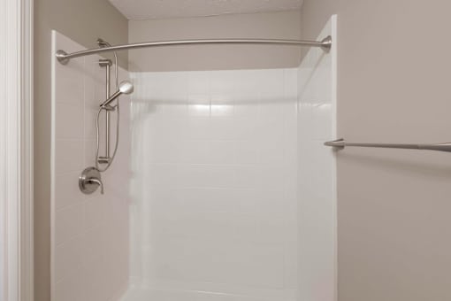 A white tiled shower with a glass door and a silver grab bar.