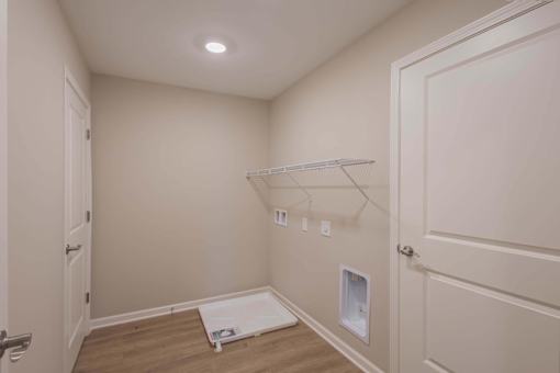 A white door is open to a room with a white shelf and a white mat on the floor.