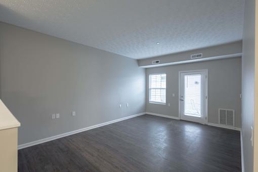A room with a door, two windows, and a light switch on the wall.