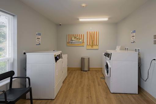 A laundry room with a washer and dryer on each side and a chair in the middle.