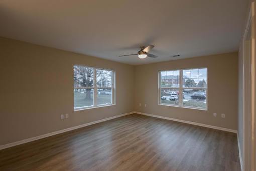 Empty room with a ceiling fan and two windows.