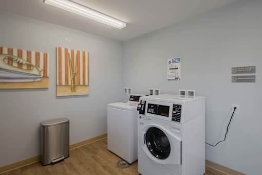 A laundry room with two washing machines and a trash can.