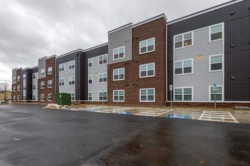 A row of modern apartment buildings with a parking lot in front.